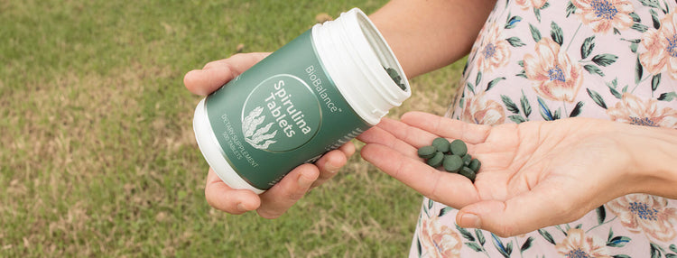 Hand pouring spirulina tablets into hand.