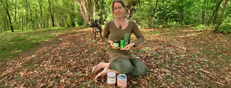 Woman sitting on the ground in a forest holding wellness products.