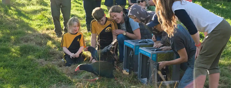 Group of people, including children, gathered around small cages in a grassy outdoor setting.