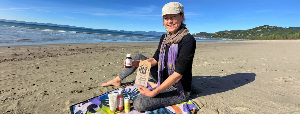 Woman sitting on a beach holding a supplement bottle and package, with a scenic background.