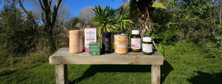 Collection of jars and bottles on a wooden table outdoors with greenery in the background.