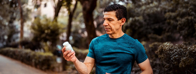 A man jogging outdoors in a blue athletic t-shirt while holding a white bottle in his hand, with trees and hedges blurred in the background.
