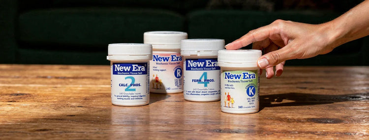 4 white bottles of New Era Tissue Salt products on a wooden bench with a person reaching.
