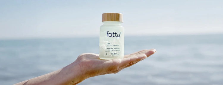 Hand holding Fatty15 C15:0 Fatty Acid Supplement in palm of hand with beach setting in the background.