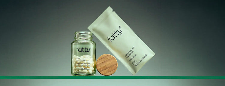 Fatty15 C15:0 Fatty Acid Supplement glass bottle on a glass surface with the wooden lid balanced next to it along with a refill pouch. Gradient background.