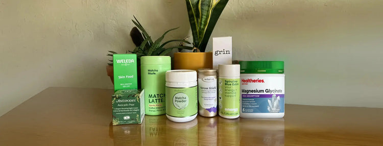 A selection of matcha, supplements & skincare on  wooden surface with some plants in the background.