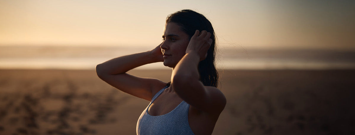 Woman running hands through hair on a beach at dawn wearing exercise gear.