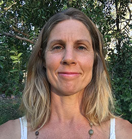 Person with long blonde hair wearing a white tank top outdoors