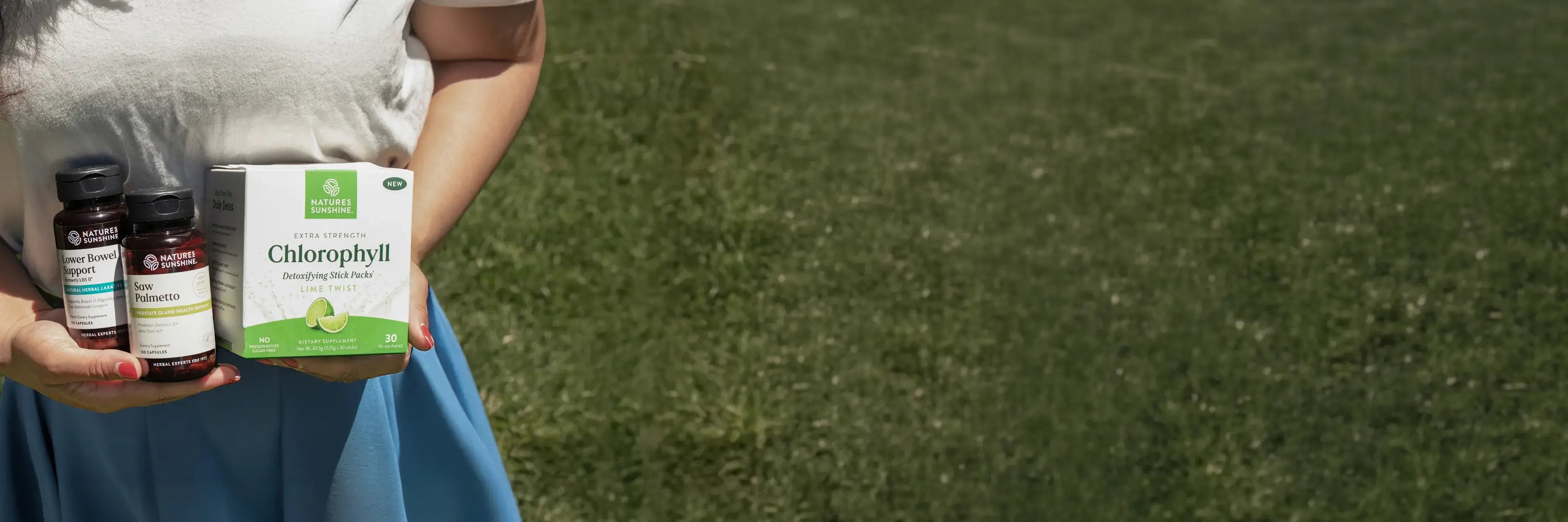 Person holding Nature's Sunshine supplement products against a grassy background.