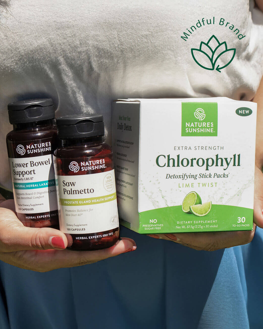 Two bottles of Natures Sunshine supplements and a box of Natures Sunshine Chlorophyll product held by a person.