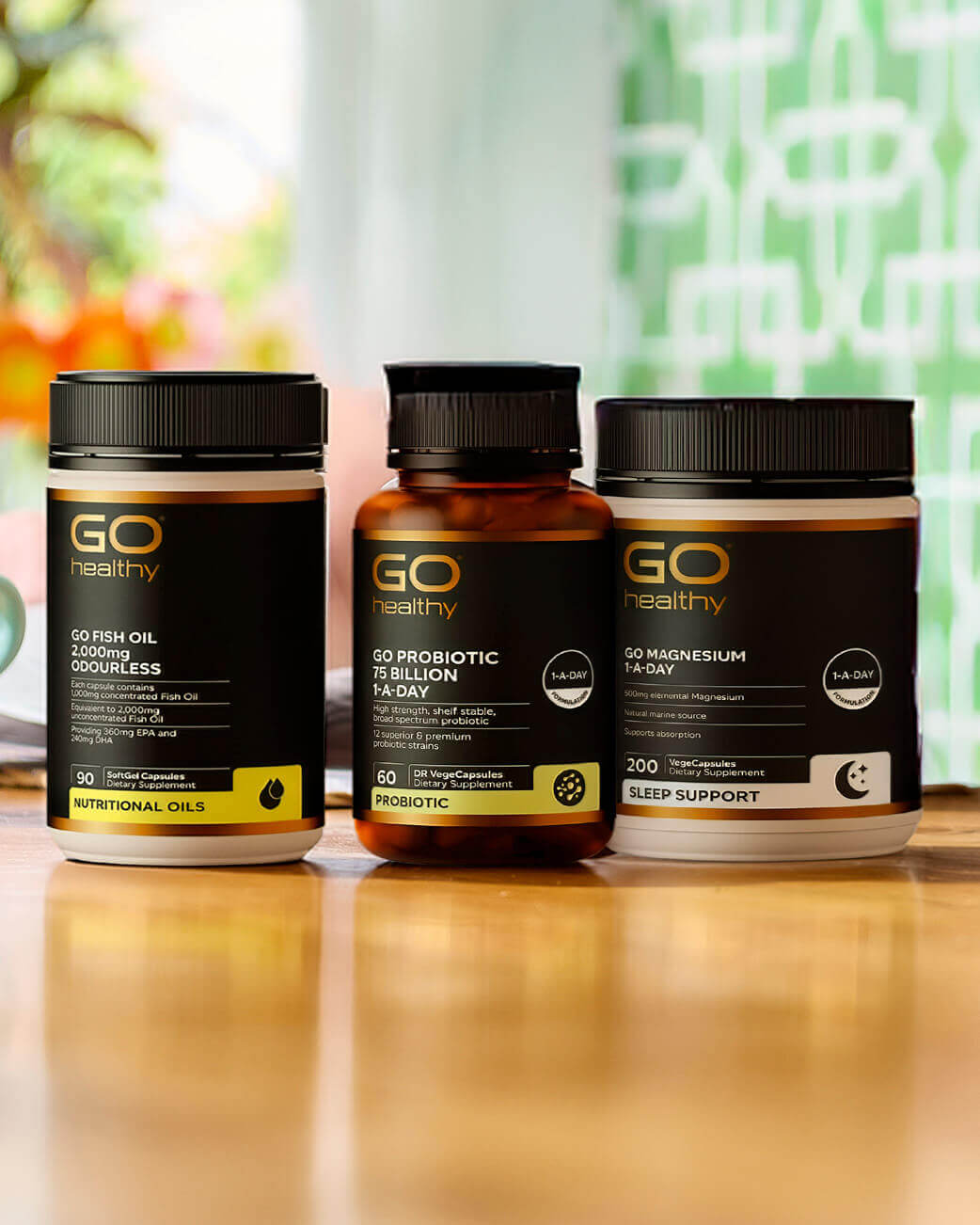 Three GO Healthy supplement bottles on a wooden surface with a blurred colourful background.