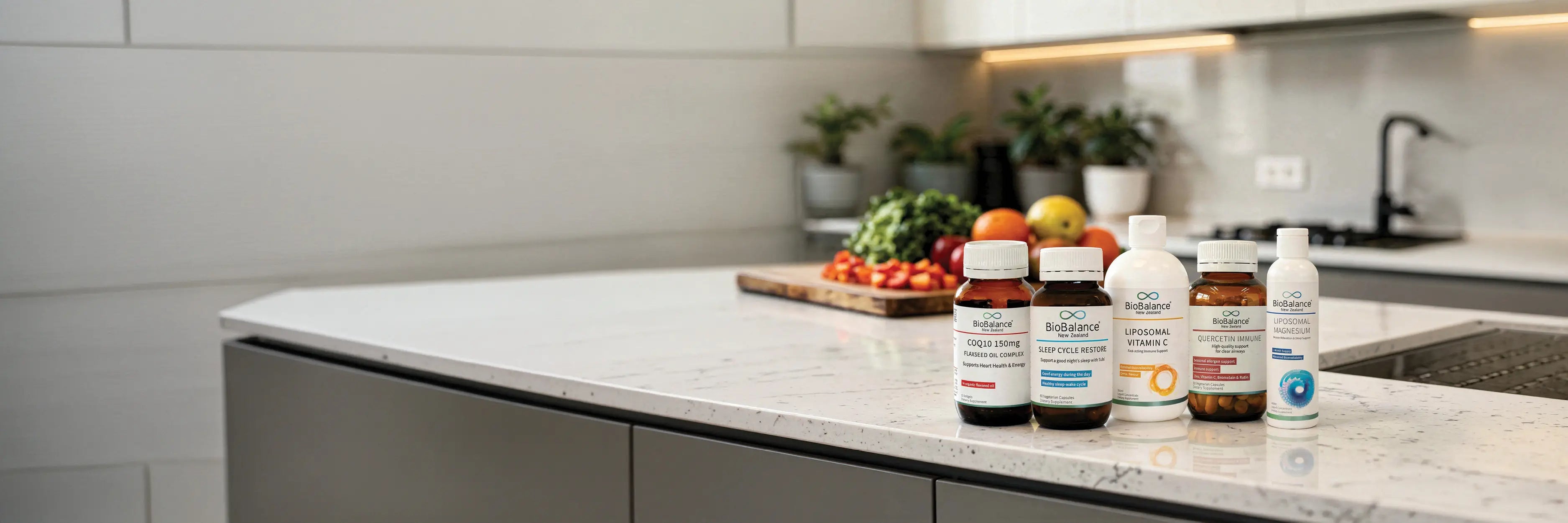 5 BioBalance products on a kitchen bench with a wooden board of chopped vegetables and fruit stacked up.