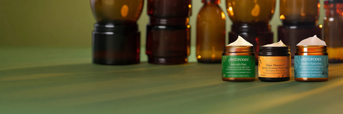 Antipodes products lined up on a green surface with empty brown bottles in the background.