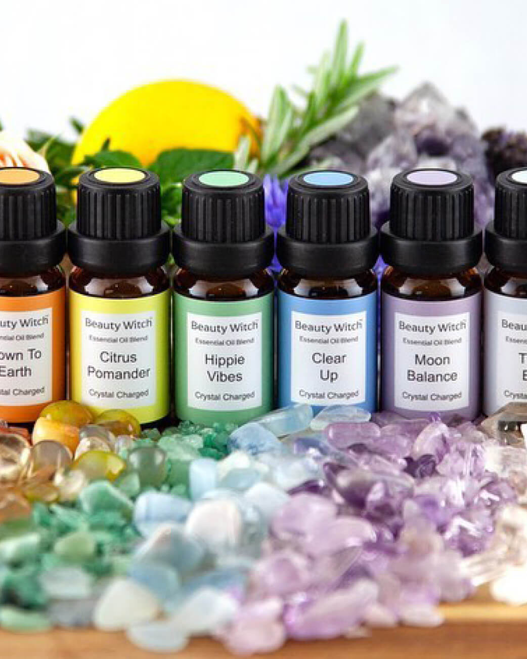 Collection of 'Beauty Witch' essential oil bottles with crystals and stones on a wooden surface.