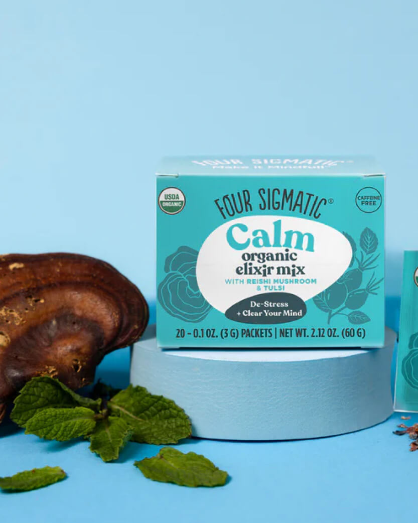 Four Sigmatic Calm organic elixir mix packaging on a blue background with mushrooms and mint leaves.