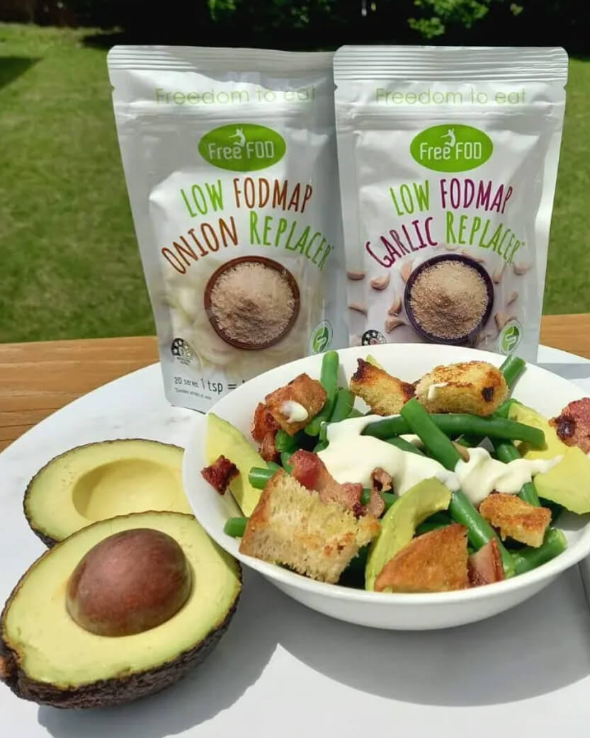 Two packages of Low FODMAP onion and garlic replacers with a salad and avocado on a table outdoors.