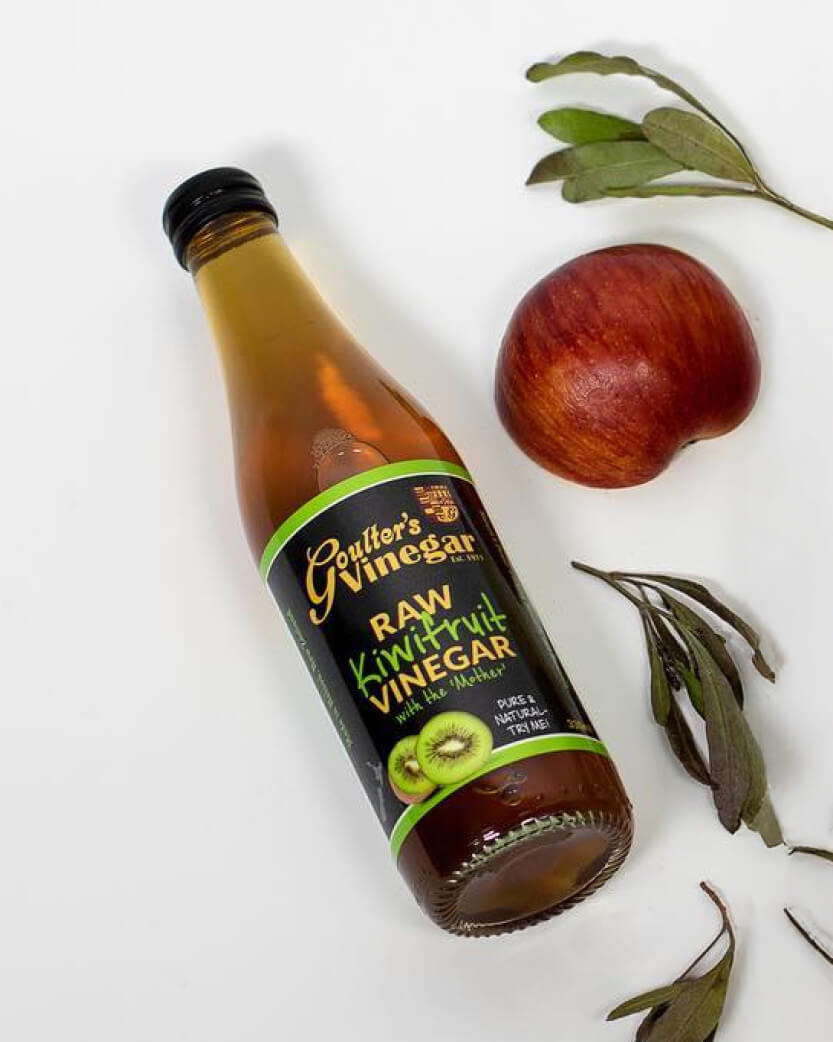 Bottle of Goulter's Raw Kiwifruit Vinegar with kiwi fruit and leaves on a white background.