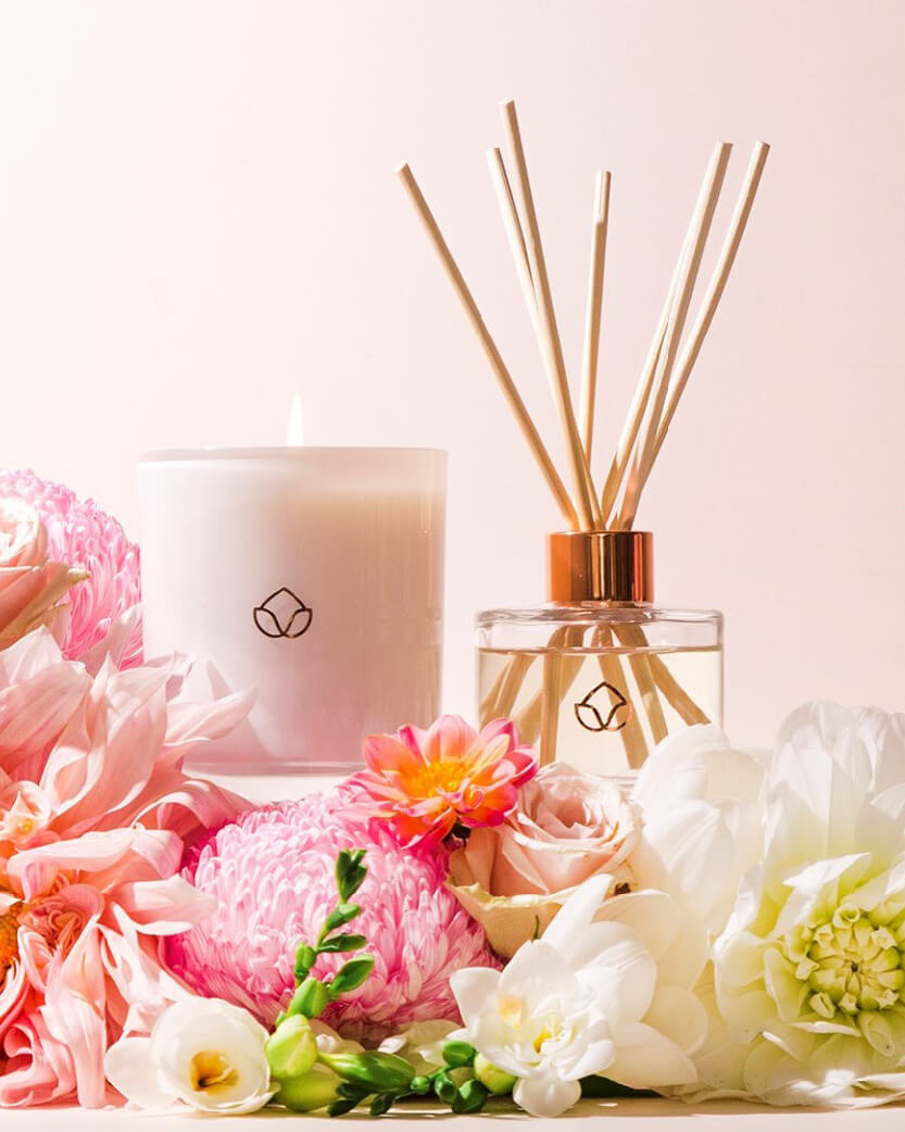 Candle and diffuser with flowers on a light pink background.