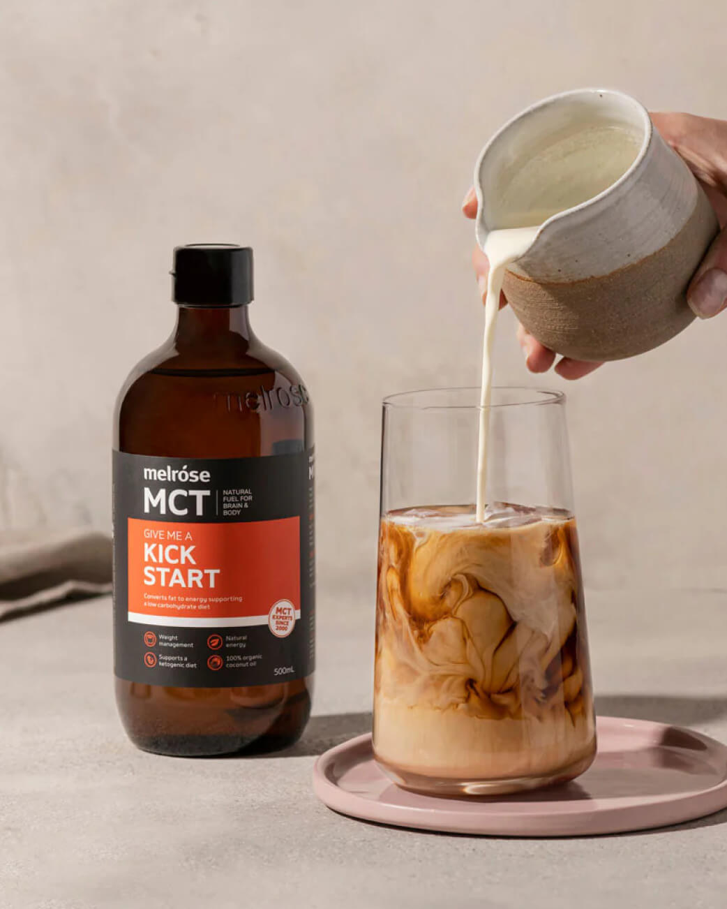 Melrose MCT oil bottle with a glass of iced coffee and milk being poured.