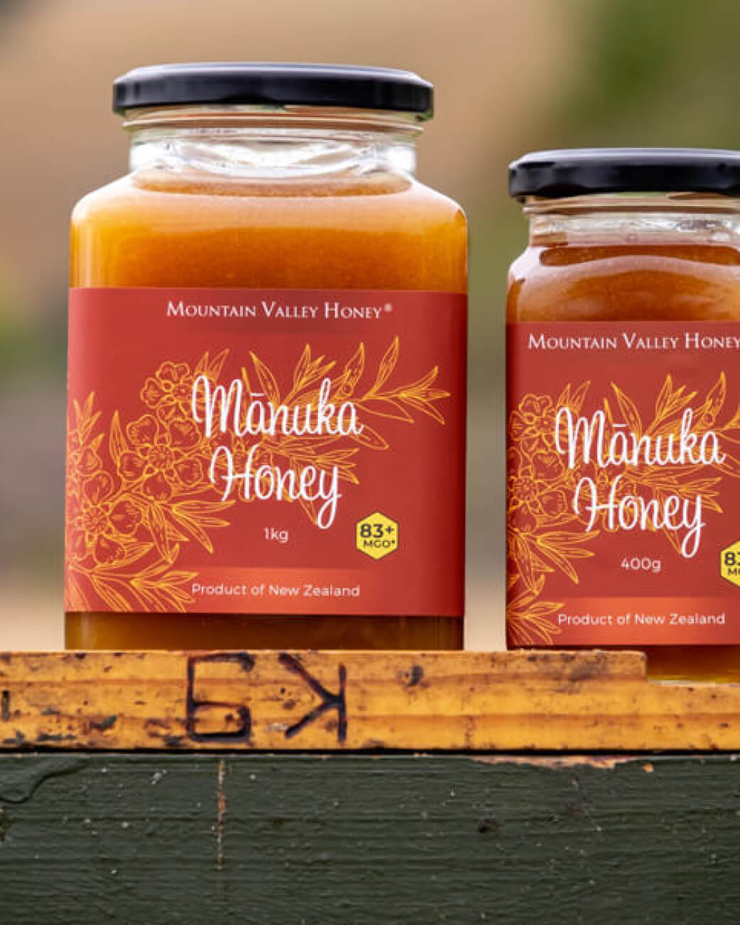 Two jars of Mountain Valley Honey Manuka Honey on a wooden surface with a blurred natural background.