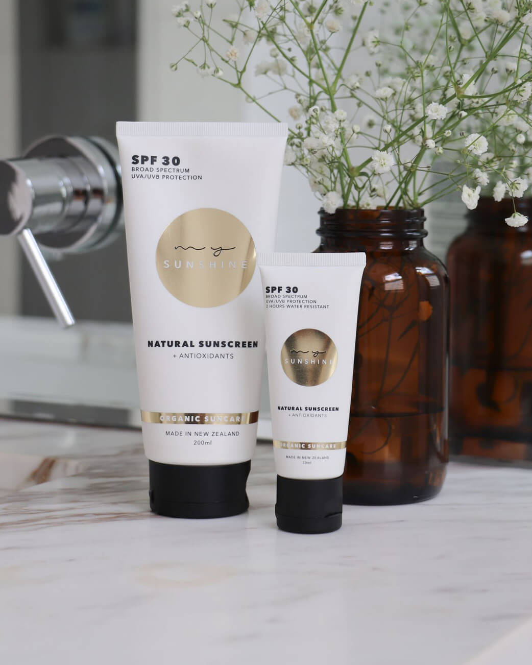 Two sunscreen tubes on a bathroom counter with flowers in the background.