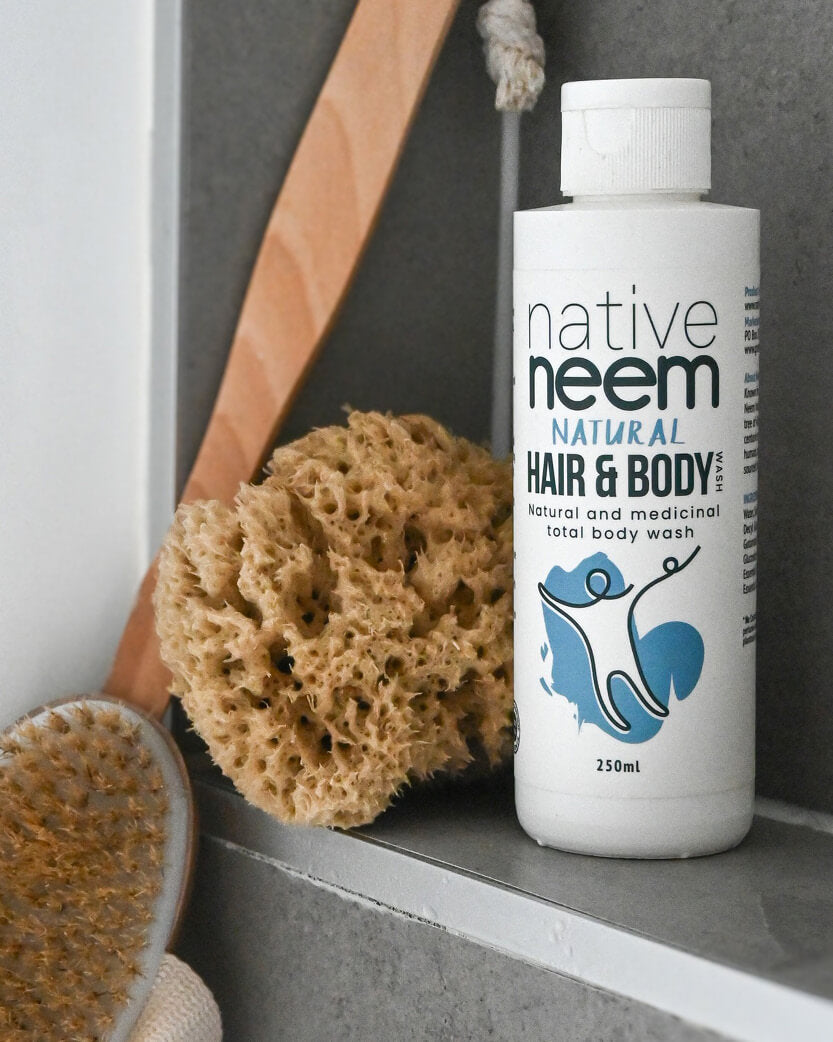 Native Neem hair and body wash bottle on a shelf with sponges and a brush.