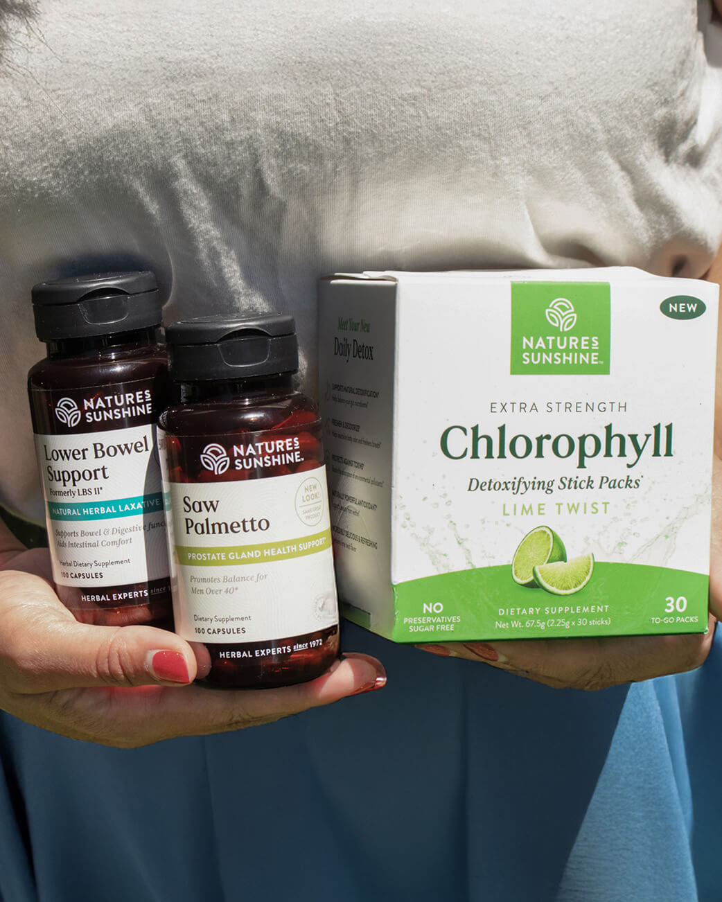 Two supplement bottles and a box of Chlorophyll sticks held by a person with a blurred background.