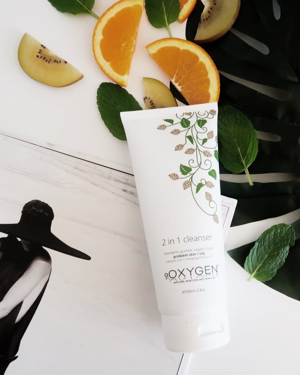Oxygen 2-in-1 cleanser tube with fruit slices and leaves on a white background.