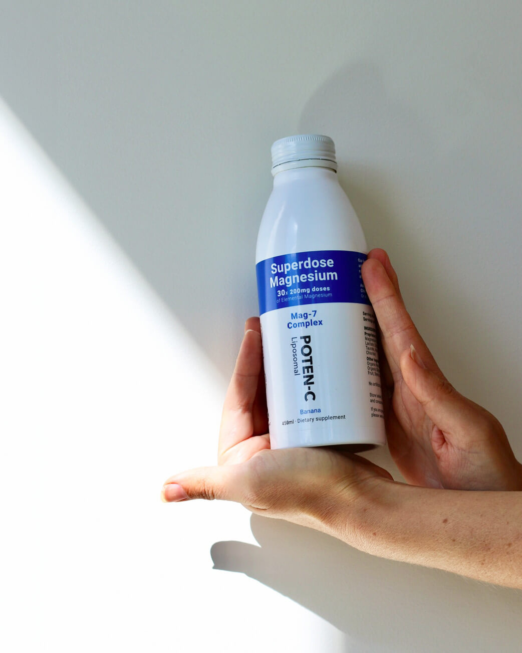 Hand holding a bottle labeled 'Superdose Magnesium' against a light background.