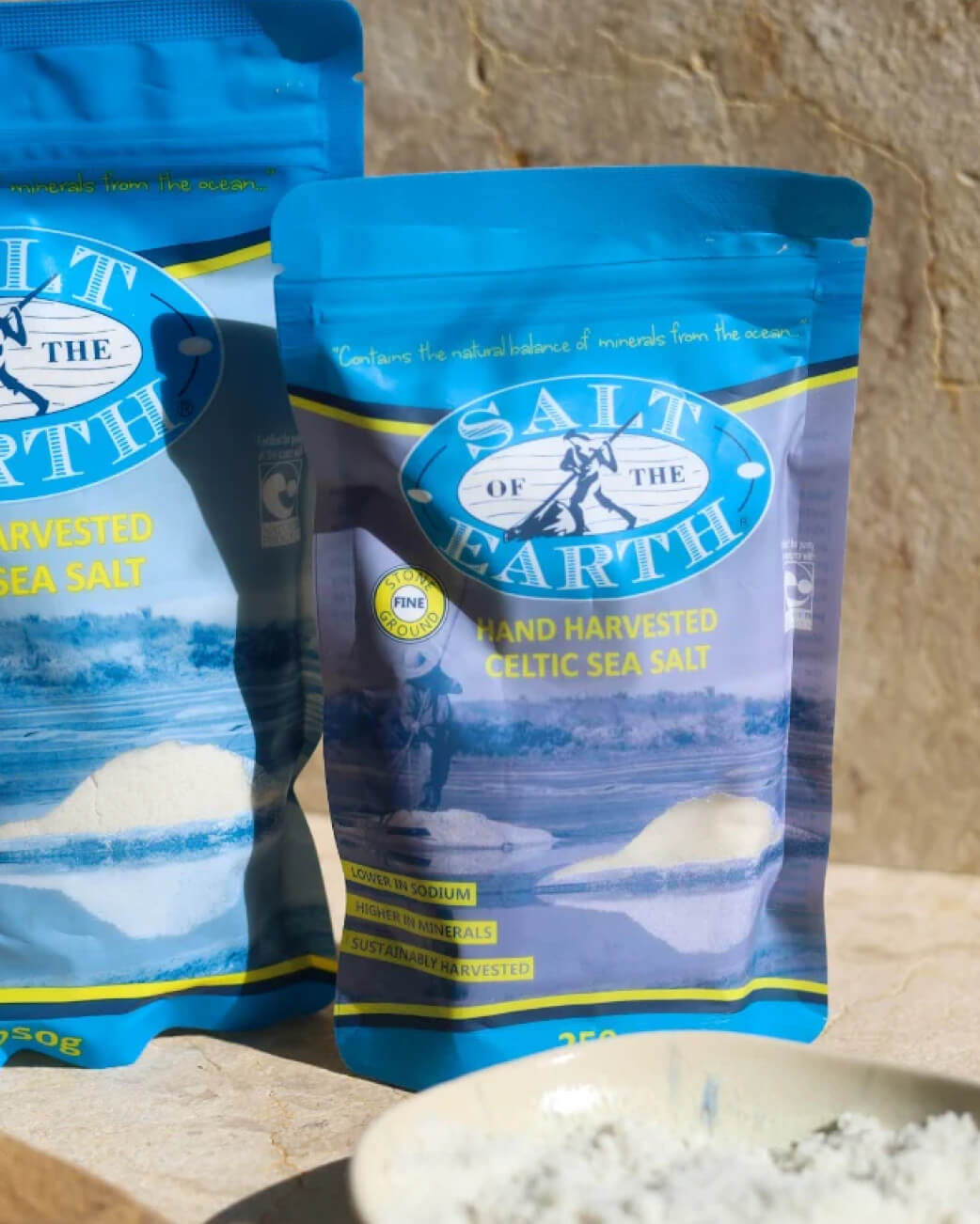 Two packages of 'Salt of the Earth' hand harvested Celtic sea salt on a wooden surface.