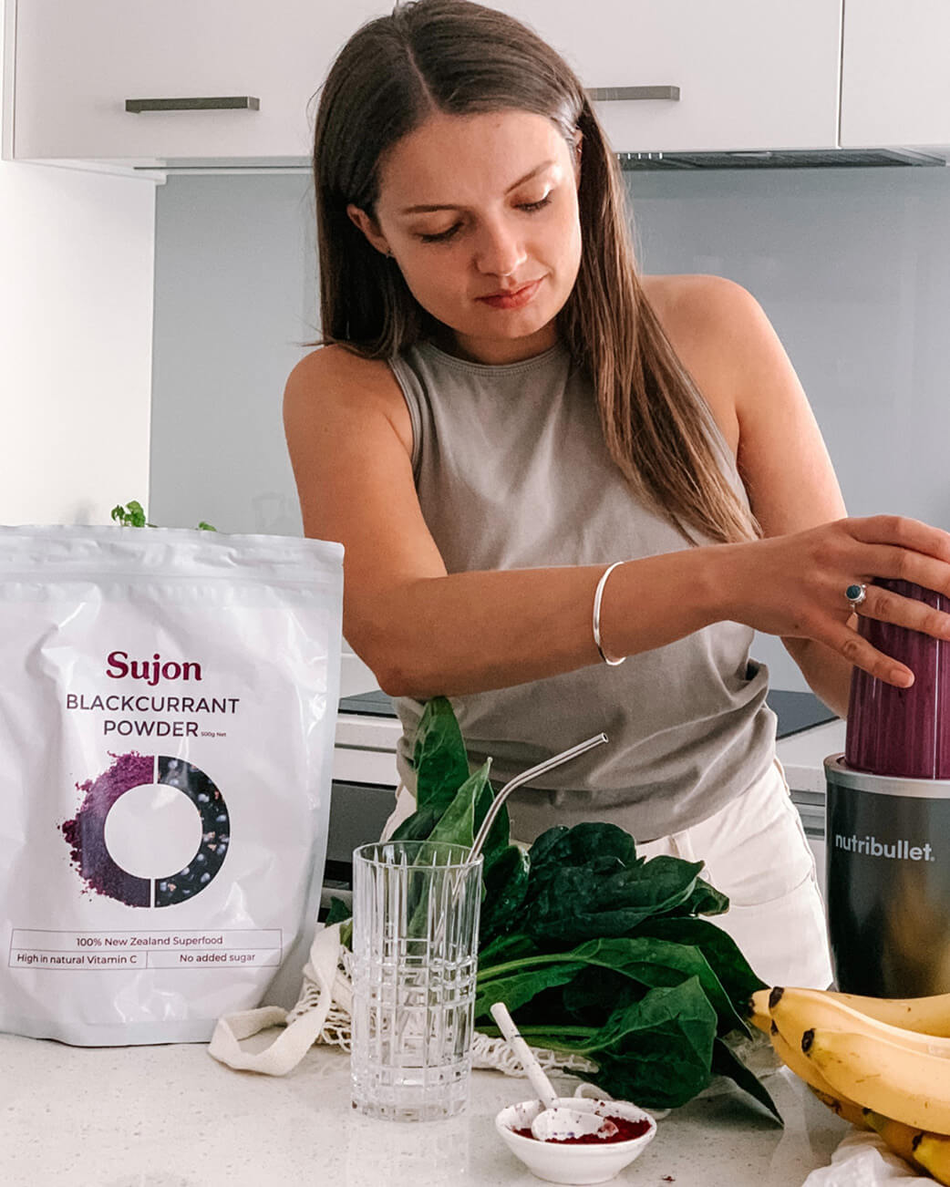 Woman preparing a smoothie with Sujon Blackcurrant Powder in a kitchen.
