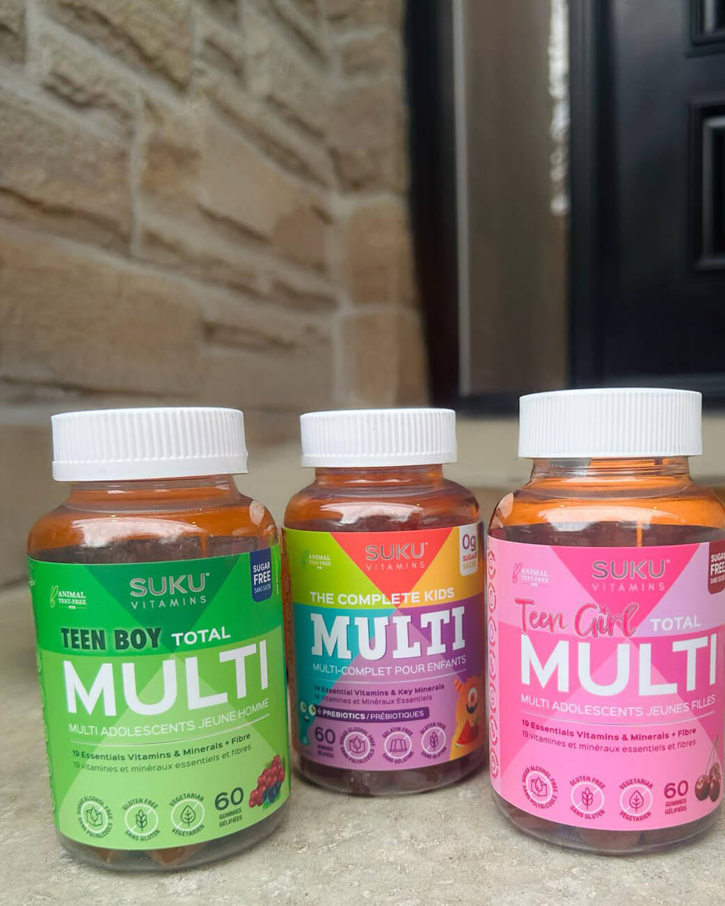 Three bottles of Suku Vitamins supplements on a stone surface with a stone wall background.