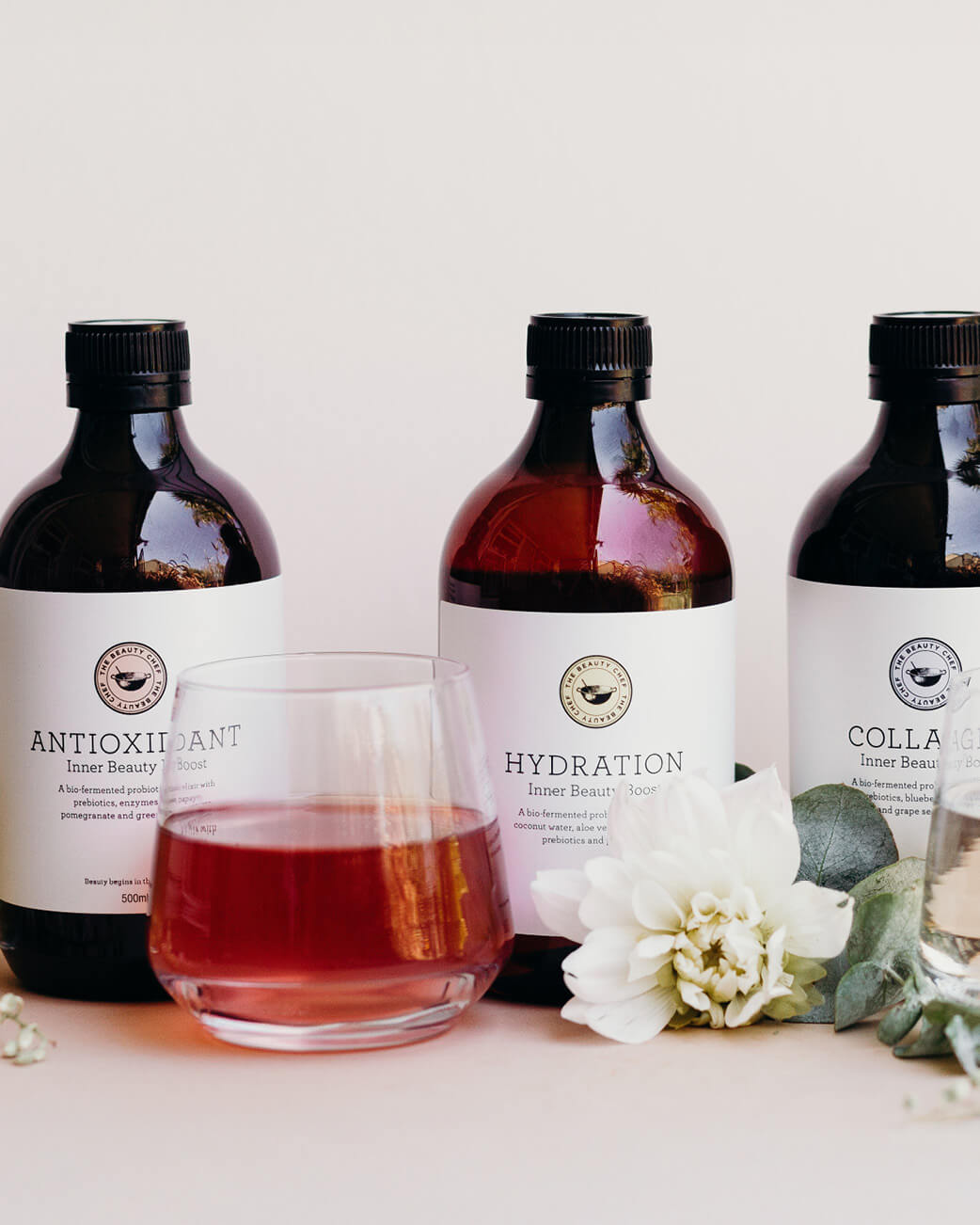 Three bottles labelled 'Antioxidant', 'Hydration', and 'Collagen' with a glass of red liquid on a white background.