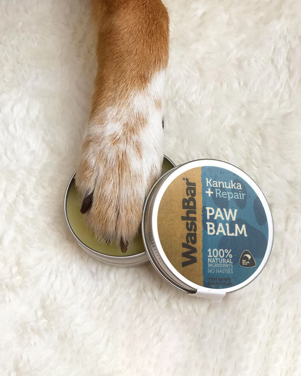 Dog paw with WashBar Kanuka + Repair Paw Balm on a white fluffy blanket.