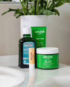 Weleda skincare products including a bottle, tube, and jar on a bathroom counter with a plant in the background.