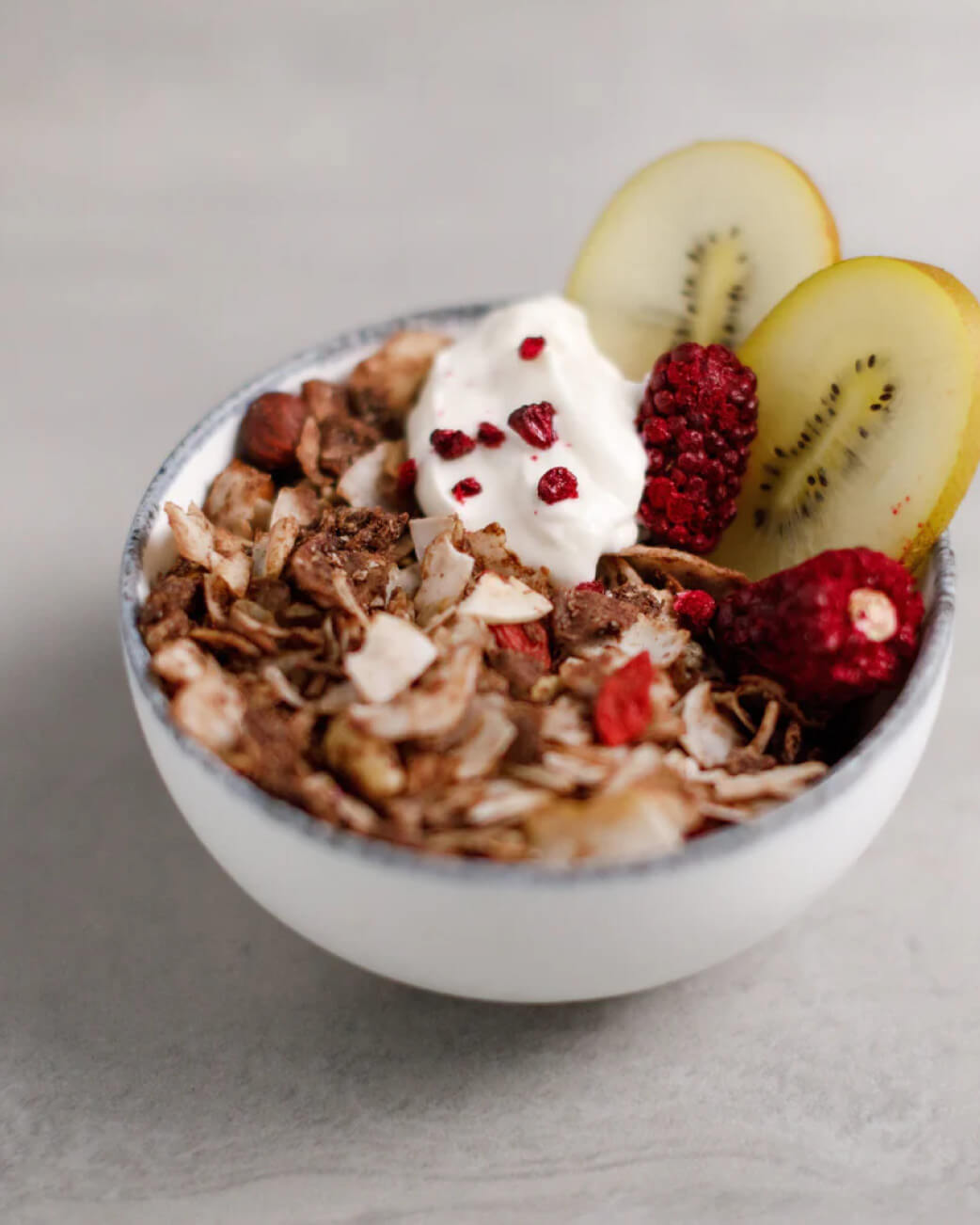 Bowl of granola with yogurt, kiwi, and berries on a light background.