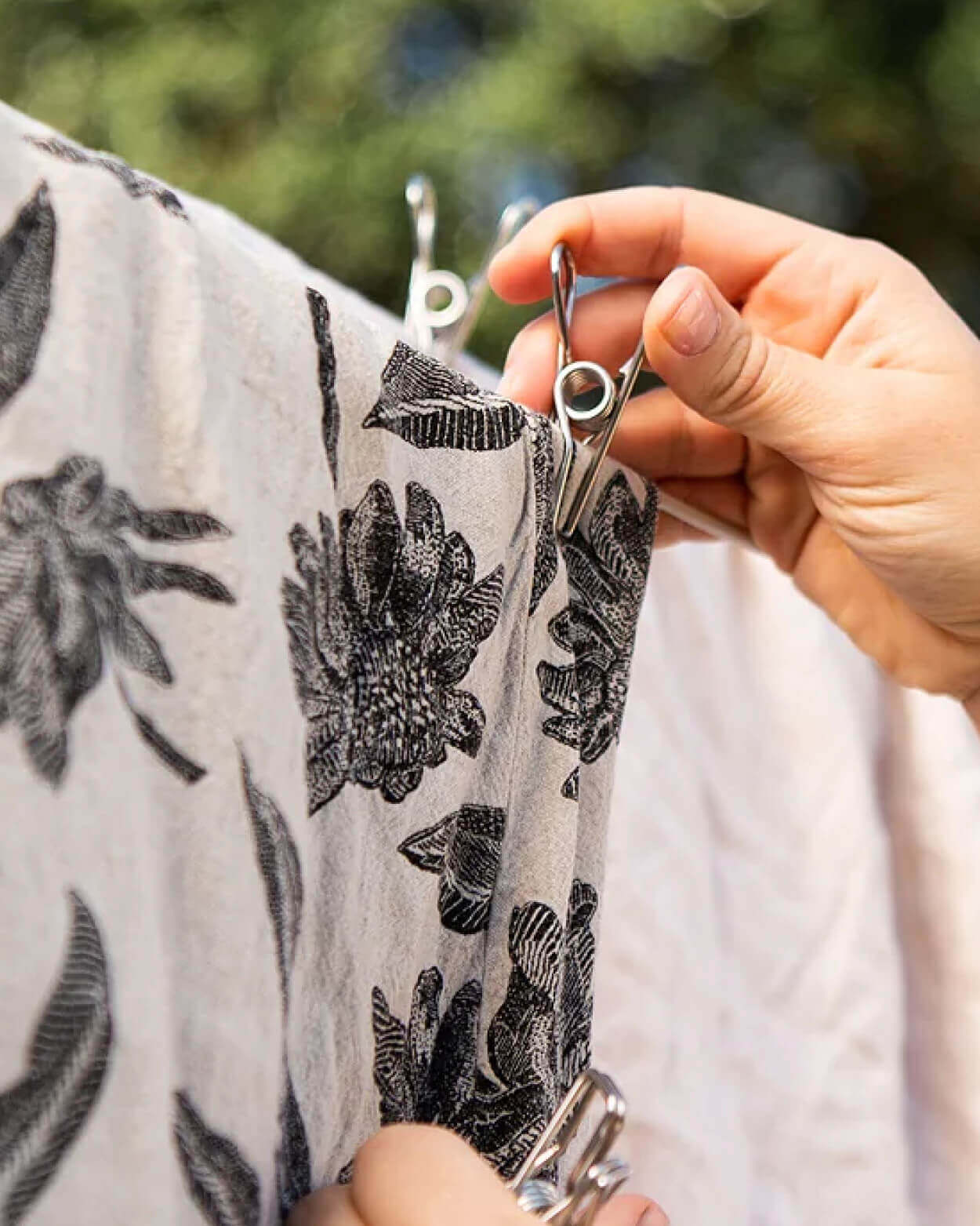 Person holding a floral-patterned fabric with a clip attached outdoors.