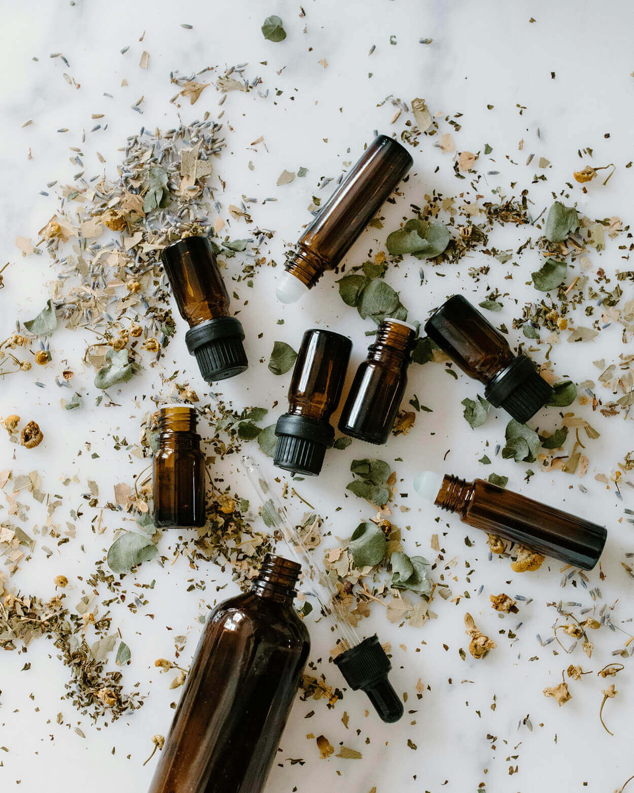 Collection of brown glass bottles with herbs and flowers on a white background.