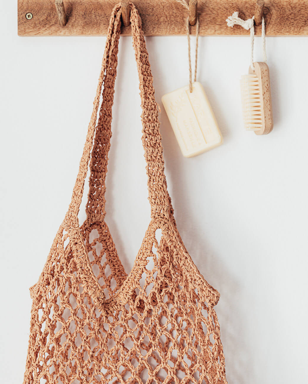 Brown crochet bag hanging on a wooden hook with a white background