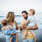 Family of four, two adults and two children, on a beach with ocean in the background.