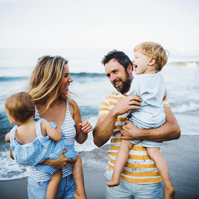 Family of four, two adults and two children, on a beach with ocean in the background.