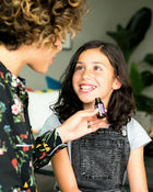 Woman showing an essential oil bottle to a young girl indoors.