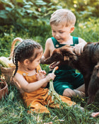 Two children sitting in a grassy area with a dog, holding carrots.