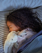 Child sleeping with a teddy bear on a striped pillow.