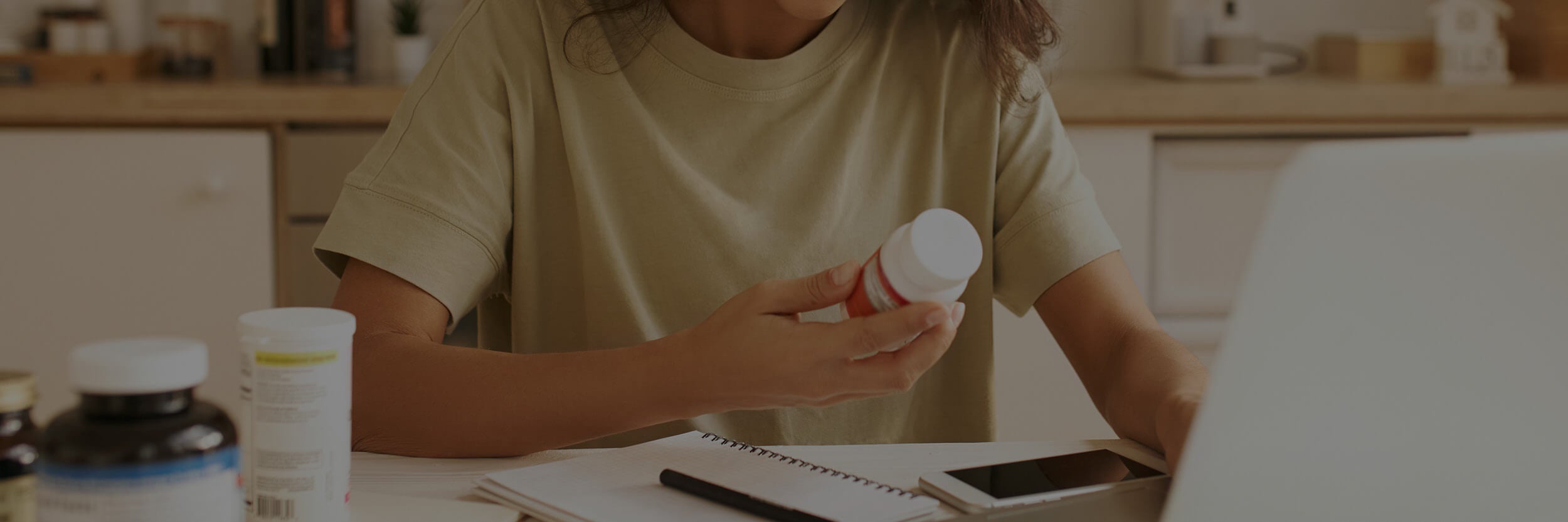 Person holding a bottle of supplements in a kitchen setting.
