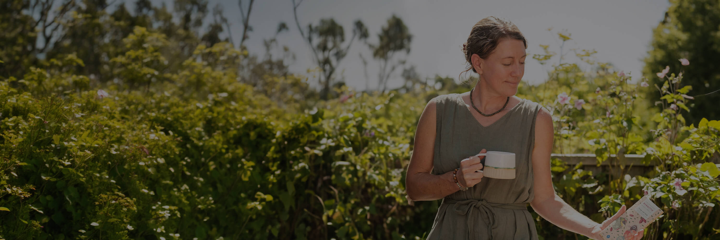 Woman holding a mug and bar of chocolate outside against a natural setting.