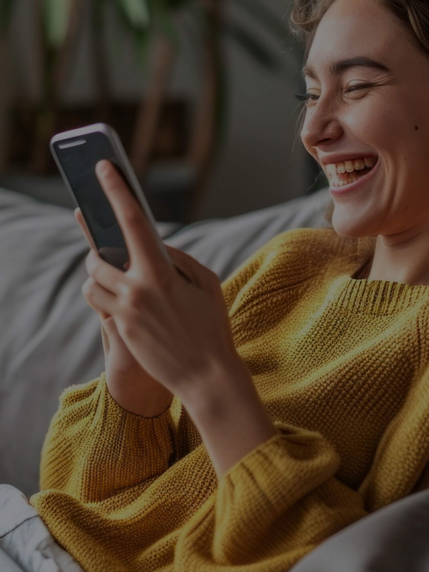 Woman in yellow sweater using a smartphone indoors.