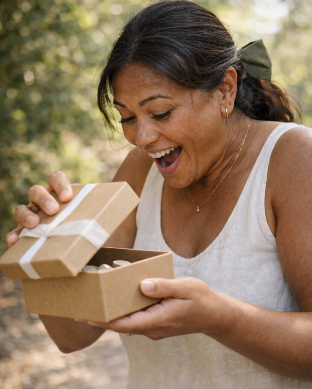 Woman opening a brown gift box outdoors with a natural background.