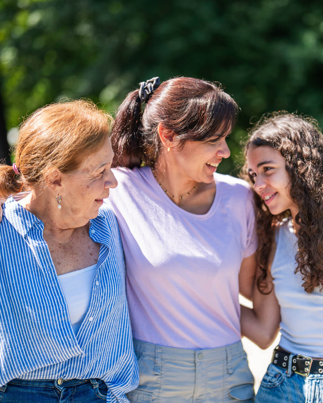 Three women standing together outdoors with greenery in the background.