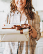Person holding a wrapped gift with a brown ribbon in a home setting.
